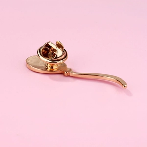 Macro shot of gold metal pin back with butterfly clasp on a soft pink background