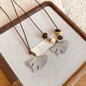 Close-up of ginkgo leaf pendants with wood beads on leather cords in a wooden tray