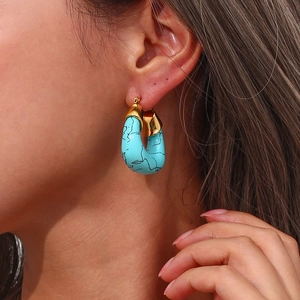 Close-up of model wearing chunky turquoise and gold crescent-shaped earrings