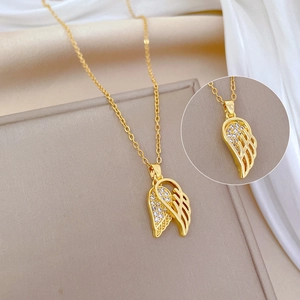 Elegant gold wing pendant necklace with crystals on beige stand and white silk