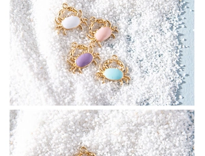 Detailed view of colorful enamel crab charms for DIY jewelry making on a sand background