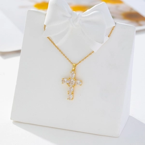 Detail of gold-plated cross pendant with clear cubic zirconia on a white bow stand