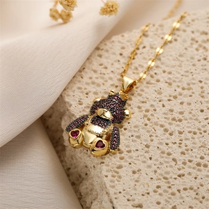 Detail of gold teddy bear pendant with red and black zircons on beige silk backdrop