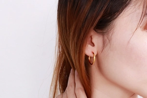 Close-up of classic minimalist 18K gold plated hoop earrings worn on a female ear model