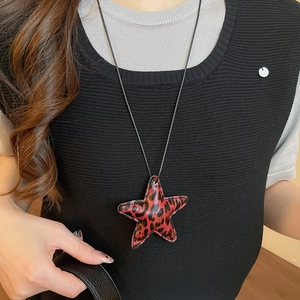 Close-up of a large leopard print star pendant necklace worn over a black sweater