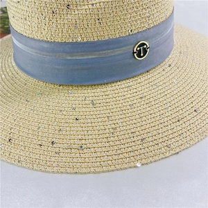 Close-up of women's straw sun hat with silver sequins, blue ribbon, and gold T logo