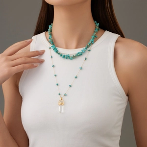 Detail of layered gold necklace with turquoise stones and a clear crystal pillar pendant