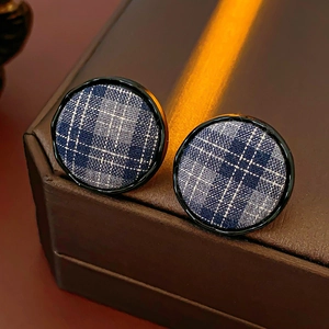 Macro view of round fabric stud earrings featuring a classic dark blue plaid pattern