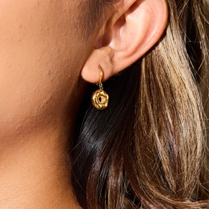 Elegant gold donut-shaped hoop earrings with lava texture on a model in sunlight