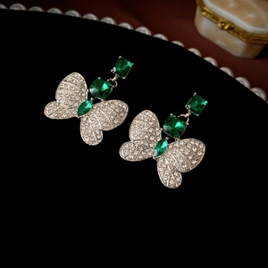 Detailed macro shot of emerald green butterfly earrings on a black velvet background