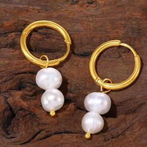 Gold hoop earrings with double pearl tassels on a rustic wood background