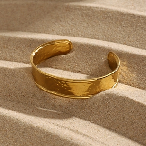 Detail of 18K gold plated wide cuff bracelet with unique hammered texture on beach sand