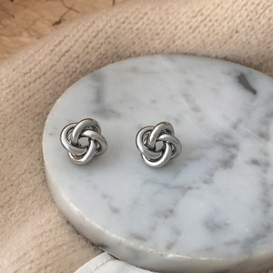 Macro detail of silver knot stud earrings on white marble tray with knit fabric texture