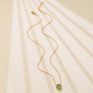 Detailed close-up of a delicate gold chain necklace featuring a round green gemstone pendant