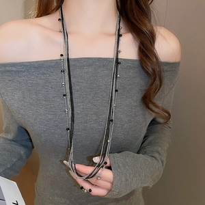 Close-up of layered silver and black beaded long necklace on a gray knit sweater