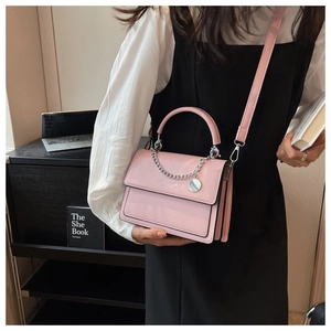 Close-up of pink crossbody bag with silver chain decoration and metallic logo tag