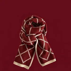 Détail d'une écharpe en tricot rouge foncé avec motif losanges ivoire et bords côtelés