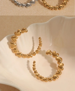 Makroaufnahme goldener Herz-Ohrringe in C-Form, präsentiert auf einer weißen Muschelschale