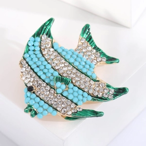 Macro shot of fish brooch showing sparkling blue beads, green enamel fins, and gold plating