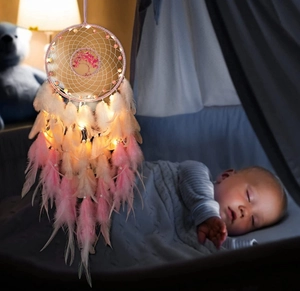 Pink and white Tree of Life dreamcatcher with feathers and glowing LED lights over a crib