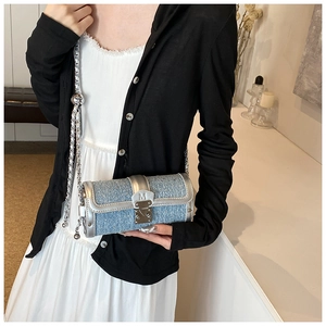 Detail of blue denim cylinder bag with silver chain strap and M-buckle on a model