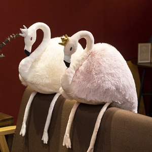 Cute white and pink plush swan dolls with shiny crowns sitting on a sofa in a warm room