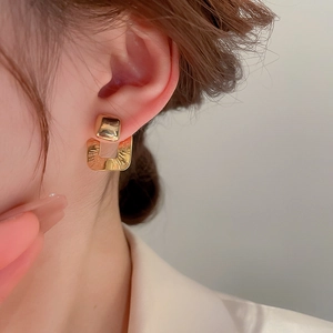 Detailed close-up of golden geometric hollow square earrings with brushed metal texture