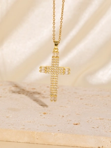 Close-up of golden cross necklace with cubic zirconia on a stone and silk background