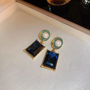 Détail de boucles d'oreilles dorées avec perles et pierre bleue dans un écrin à bijoux