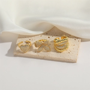 Three vintage gold flower and heart zircon adjustable open rings on a beige stone background