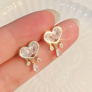 Detail of a gold heart stud earring featuring clear cubic zirconia and a liquid drop fringe