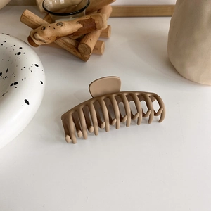 Detail of matte khaki hair claw clip on white surface with minimalist decor