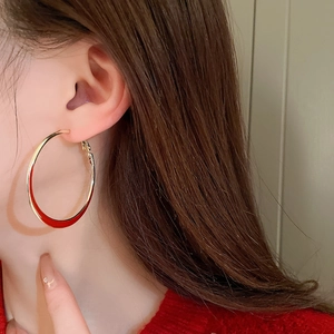 Close-up of model wearing large gold-rimmed red enamel hoop earrings for a vintage look
