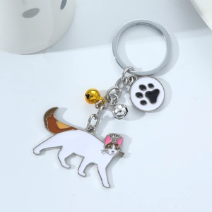 Detail of white enamel cat keychain with golden crown, paw tag, and colorful bells