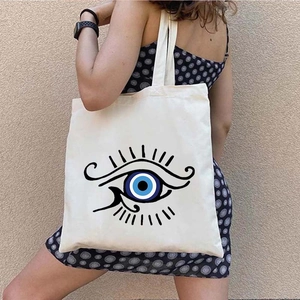 White canvas tote bag featuring graffiti Greek Evil Eye print shown on a model's shoulder