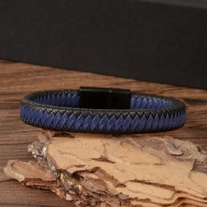 Detail of blue and black braided leather bracelet with black magnetic clasp on wood