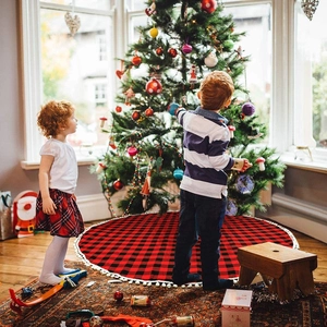 Weihnachtsbaumdecke mit rot-schwarzem Karomuster, weißen Pompons und gemütlicher Atmosphäre