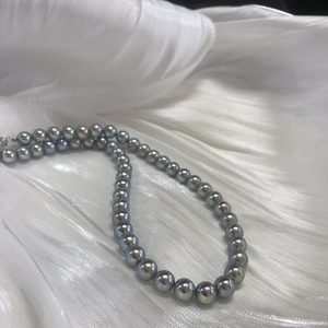 Close-up of aurora Akoya style silver-blue pearl necklace on elegant white silk fabric