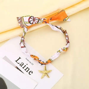 Vue détaillée du collier foulard en soie orange avec un pendentif étoile de mer doré