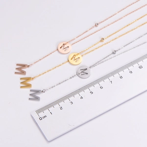 Detail of three-color letter M necklaces with zircon accents and measurement scale