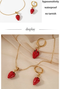 Detail of waterproof gold strawberry necklace and earrings set on soft textured cloth