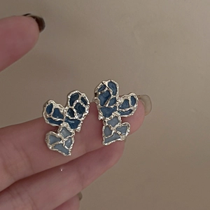 Detailed close-up of gold-plated heart stud earrings with blue enamel patterns