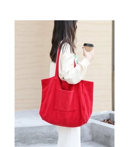 Large red corduroy tote bag showing soft ribbed texture and front pocket on model