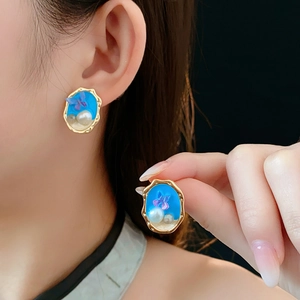 Dettaglio di orecchini vintage in oro con smalto blu, farfalla e perla su una modella