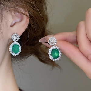 Détail des boucles d'oreilles émeraude avec zircons blancs en forme de soleil