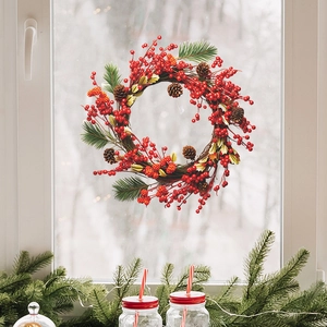 Christmas wreath with red berries and pine cones hanging on a window for home wall decor