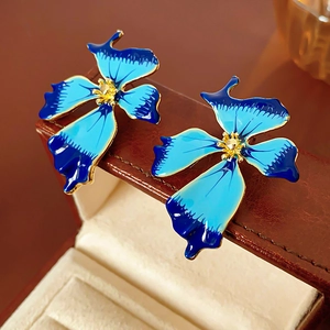 Macro shot of blue enamel flower earrings with gold trim on a brown leather jewelry box