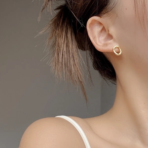 Close-up of minimalist golden oval earrings worn on the ear showing high-quality texture