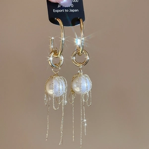 Detail of golden tassel earrings with round pearls and delicate metallic bead chains