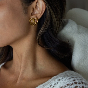 Détail de boucles d'oreilles cœur torsadées en acier doré portées par un mannequin
